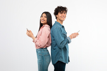 Smiling Young Couple Using Smartphones Posing On White Studio Background