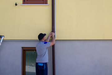 Image of a handyman on a stepladder assembling a gutter channel. Do-it-yourself jobs and home maintenance.
