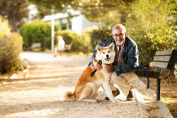 Smiling european old man in casual and glasses enjoy walk with dog and spare time, hugs in park,...