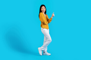 Fototapeta na wymiar Cheerful beautiful korean woman showing thumb up, blue background