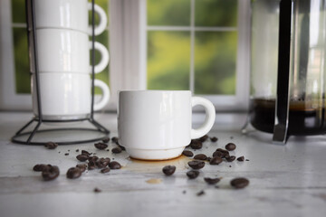 Cup of coffee with coffee beans scattered kitchen window in the background