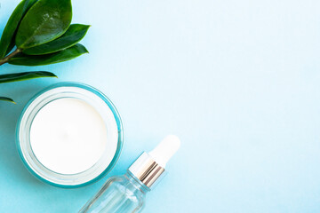 Natural cosmetic, cream jar with green leaves on blue. Flat lay with copy space.