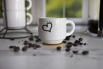 Small espresso cup with a heart on it scattered coffee beans by a kitchen window
