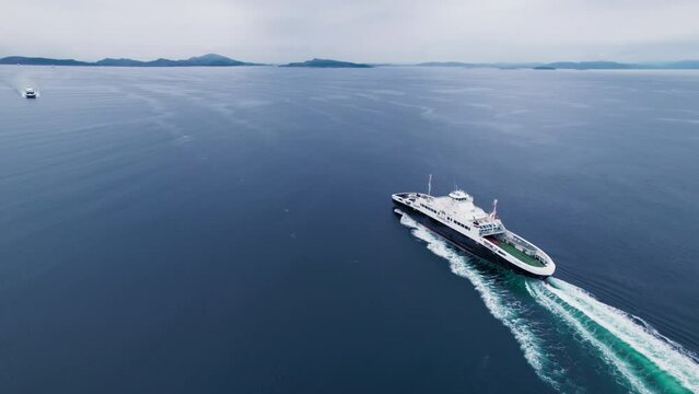 Drone shot of passenger and vehicle ferry cross fjord or move between islands in Norwegian archipelago. Naval transportation and logistics concept