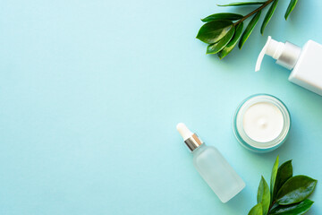 Natural cosmetic products. Cream, serum, tonic with green leaves. Flat lay on blue.