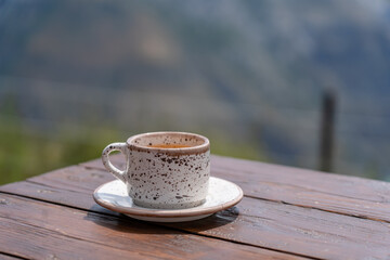 Motley coffee cup on shabby wooden table with green nature mountainside background