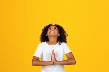 Smiling adolescent curly girl in white t-shirt looking up, praying gesture
