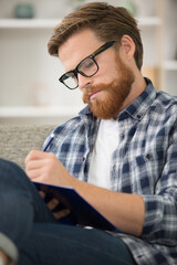 intelligent man writing in book sat on the sofa