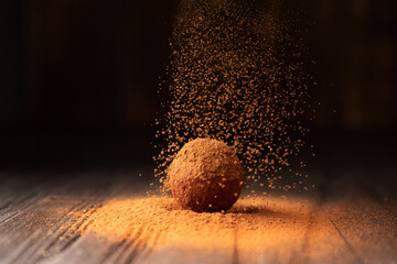 Delicious chocolate truffles sprinkled with cocoa on a black reflective background.
