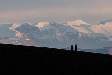 Fototapeta na wymiar A very distant couple shaking hands on top of a mountain with distant hills and mountains covered by snow