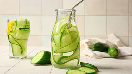 Bottle and glass of cucumber infused water on light table