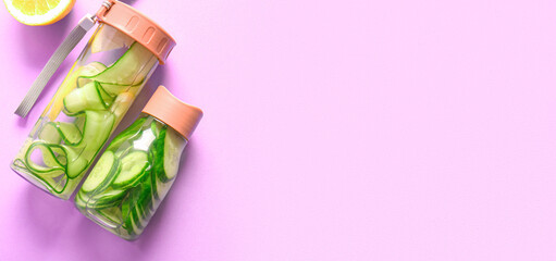 Bottles of cucumber infused water on lilac background with space for text