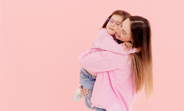 A young mother has fun playing with a cute little daughter, holding in her arms, gently hugging on a pink background