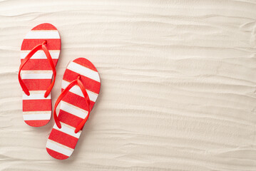 An aerial glimpse of summer bliss. Red and white striped flip-flops rest harmoniously on the sandy beach. Embrace the empty space for text or adverts