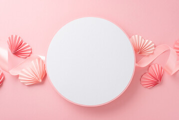 Top view photo of empty white circle with a pastel pink ribbon and paper origami hearts on an...