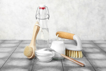 Bottle of vinegar, baking soda and cleaning brushes on grunge tile table