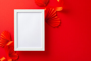 Top view photo of white empty frame surrounded by bright red ribbon and paper origami hearts on...