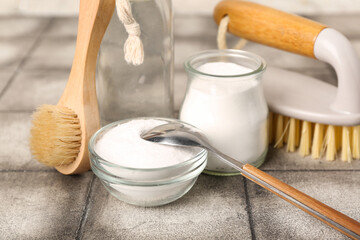 Bowl of baking soda and cleaning brushes on grunge tile table, closeup