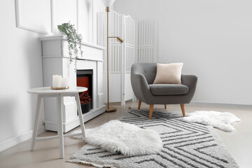 Cozy grey armchair with cushion, fireplace and folding screen in interior of living room