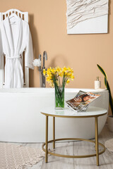 Interior of bathroom with bathtub and narcissus flowers on table