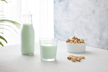 A glass of plant-based nut milk is on the table next to a bottle of pistachio milk and pistachios. The perfect drink for vegans.