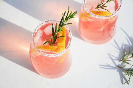 Top view of fresh grapefruit or red orange cocktails, with ice cubes, fresh fruit slices inside and rosemary. Vacation and summer cocktails concept. Citrus drink.