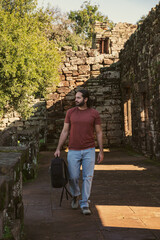 Fototapeta na wymiar Alone male tourist in jeans, red shirt, backpack and long hair walking through the ruins of San Ignacio Mini. Ruins of Jesuit missions in Argentina.