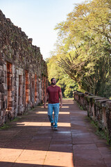 Fototapeta na wymiar Alone male tourist in jeans, red shirt, backpack and long hair walking through the ruins of San Ignacio Mini. Ruins of Jesuit missions in Argentina.