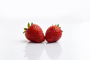 Two ripe juicy strawberries with leaves on a white background with a reflection on the table and space for text