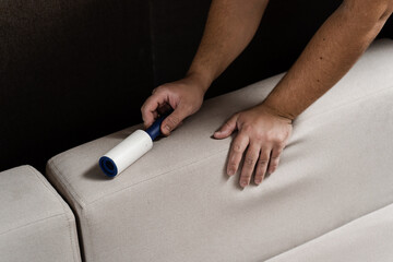 Cleaning couch using lint roller from cat and dog hair. Cleaner is removing lint from sofa using cleaning roller close-up.