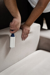 Cleaning couch using lint roller from cat and dog hair. Cleaner is removing lint from sofa using cleaning roller close-up.