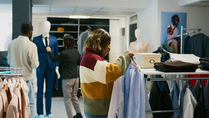 Modern client looking at shirts hanging in clothing store, young woman shopping for formal clothes to increase wardrobe. Shopping center customer buying modern fashion collection.