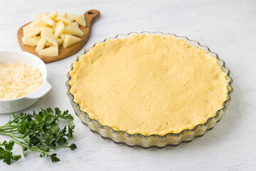 Raw polenta in a baking dish, two types of cheese and parsley on a light gray background. Stage of cooking delicious Italian polenta