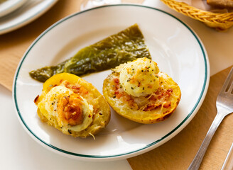 Baked potato in jacket loaded with cheese and topped with bacon and fried egg on plate with pepper. Stuffed potato with topping