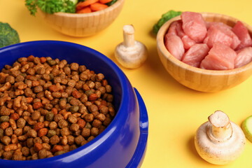 Bowls with dry pet food, raw meat and natural products on yellow background, closeup
