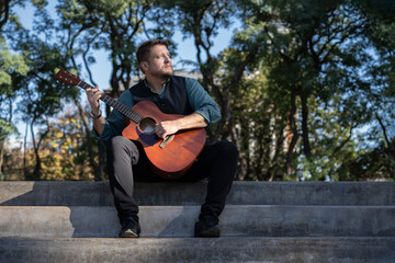 Naklejka premium Guitarist sitting in a park playing his guitar