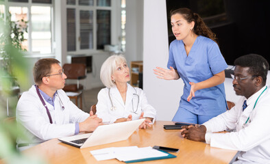 Obraz premium Young female doctor speaks at meeting of colleagues and tells reports on work done in clinic. Medical workers and colleagues participate in discussion and make suggestions and amendments