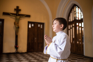 a boy before first Eucharist in a catholic church. child in white clothes in church