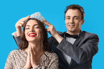 Young man crowning his prom date on blue background, closeup
