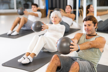 Willing middle-aged man engaging in pilates training with ball in gym room during training session