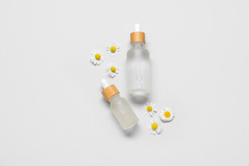 Bottles of essential oil and chamomile flowers on white background