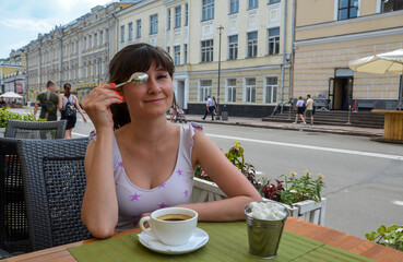 
Сheerful girl in a street cafe drinks fresh fragrant coffee, and fools around covering her eyes...