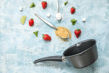 Saucepan and ingredients for preparing strawberry compote on blue background