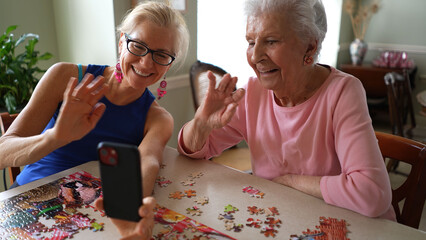 Happy waving and smiling, laughing elderly senior woman sitting at table with mature middle aged...