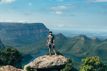 Man on a cliff  looking off into the distance with a the view from the top of the Blyde river...