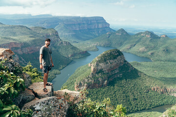 Obraz premium Man on a cliff looking off into the distance with a the view from the top of the Blyde river canyon in South Africa.