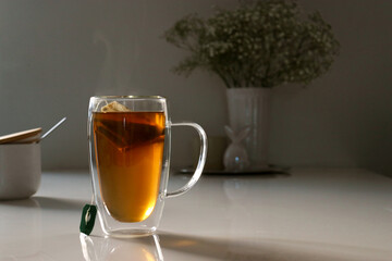 black tea in a glas cup on white table, flower in background with copy space