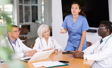 Fototapeta premium Group of different people medics in medical uniforms having discussion about work at table in office