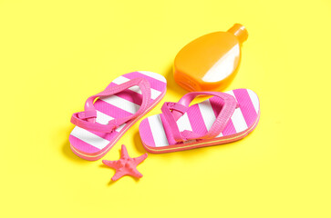 Bottle of sunscreen cream with starfish and flip flops on yellow background