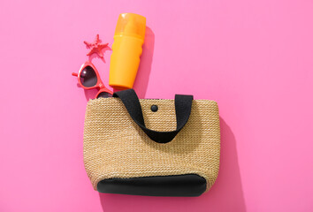 Bottle of sunscreen cream with sunglasses and wicker bag on pink background